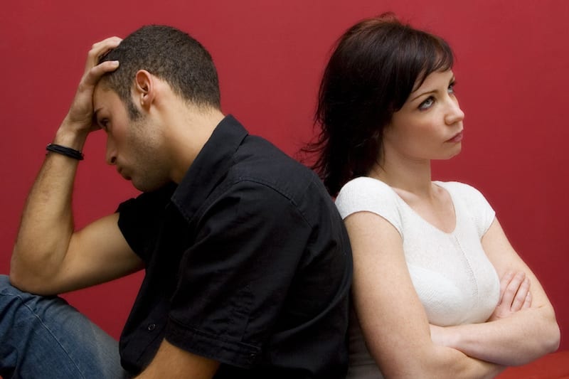 Woman and man sitting back to back on bed