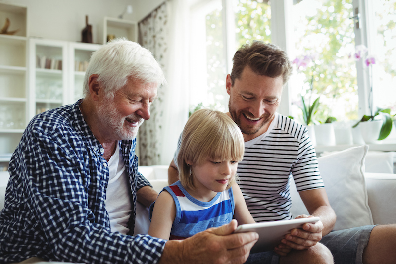 Boy using digital tablet with his father and grandfather in living room at home